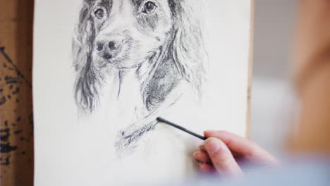 primer plano del artista sentado en el caballete dibujando una imagen de perro en carbón