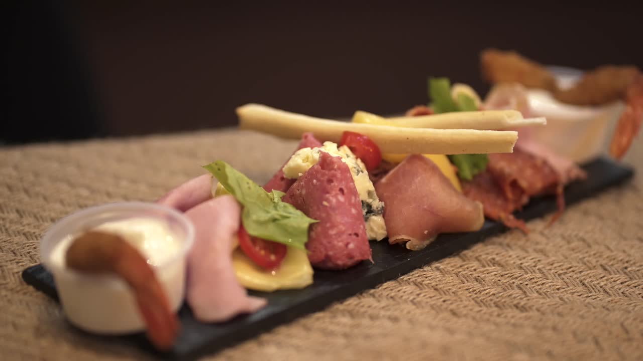 A delicious assortment of cold cuts, salami, ham, and cheese served on a slate platter with breadsticks