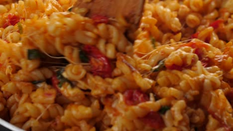 Mouthwatering-close-up-shot-in-slow-motion,-stirring-creamy-and-cheesy-pasta-in-tomato-sauce-using-wooden-spatula,-stretching-melted-mozarella-cheese