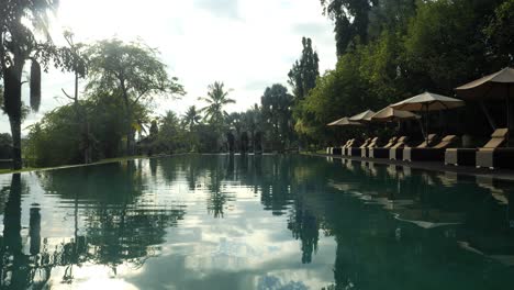 Zeitlupenaufnahme-Eines-Pools-Auf-Bali,-Indonesien,-Mit-Blick-Auf-Den-Wunderschönen-Morgen,-Sonnenliegen-Und-Bäume-Im-Hintergrund-Während-Einer-Traumhaften-Reise