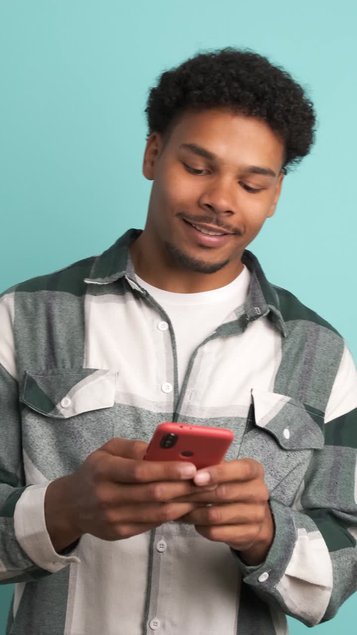Cheerful young man using smartphone in blue studio