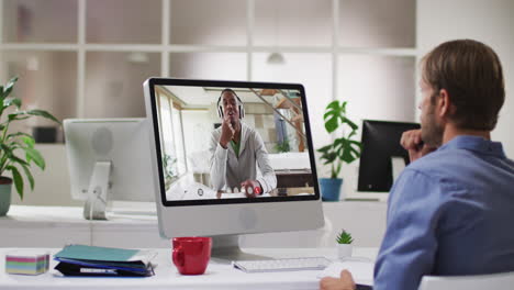hombre de negocios caucásico sentado en un escritorio usando una computadora haciendo una videollamada con un colega masculino