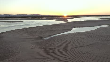 El-Sol-Arde-En-El-Horzion-Durante-La-Puesta-De-Sol-Mientras-El-Dron-Vuela-Hacia-Atrás-Para-Revelar-Una-Hermosa-Playa-Dorada