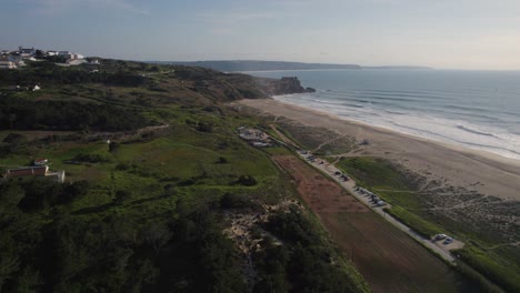 Landschaft-Von-Nazaré-Mit-üppigen-Grünen-Hügeln-Mit-Bäumen,-Den-Weißen-Gebäuden-Des-Dorfes-An-Der-Küste-Und-Dem-Atlantischen-Ozean