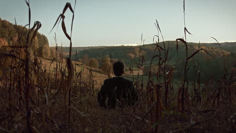 a young man sits in the middle of the corn field in late autumn and lays down on the ground to look at the sky