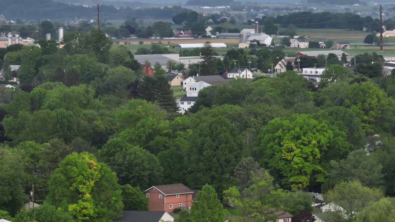 American suburb neighborhood with houses between green trees in spring. Cloudy day in rural area of town. Farm houses and farmstead in distance. Drone Tilt up wide shot