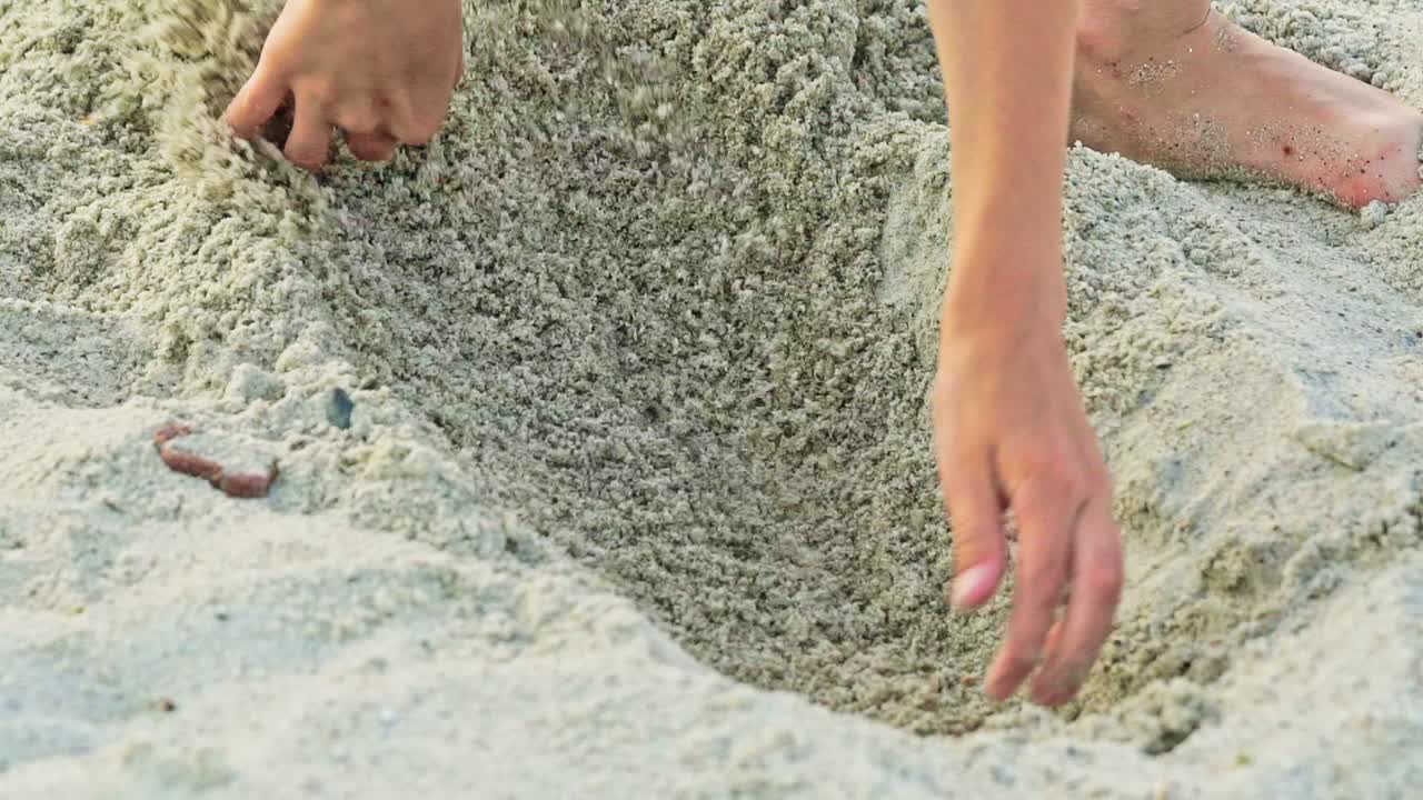 A little boy in a plaid shirt digs a bay with his hands on a sandy beach in the summer. Children's games. Close-up.