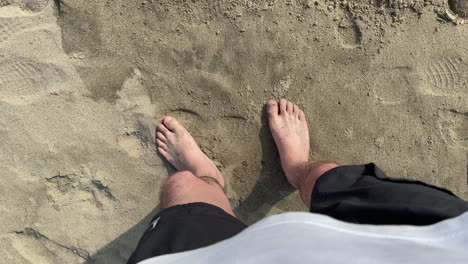 looking down at legs and feet without shoes of a male person standing on a beach