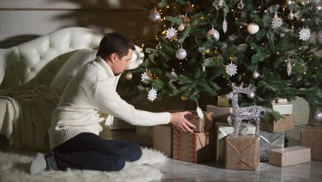 man opening christmas gifts by the christmas tree