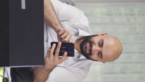 el video vertical del hombre trabajando desde casa disfruta de aplicaciones móviles en el teléfono.