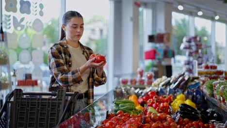 Concentrated-brunette-girl-in-a-checkered-shirt-chooses-red-tomatoes-in-the-vegetable-section-of-the-supermarket