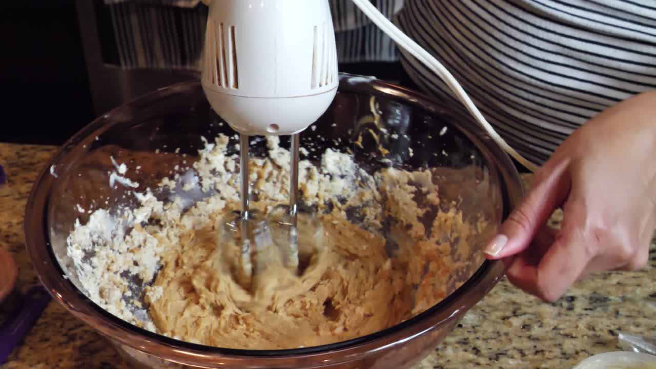 Female in kitchen mixing cooking dough ingredients in glass bowl with mixer appliance