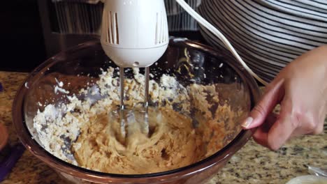 female in kitchen mixing cooking dough ingredients in glass bowl with mixer appliance