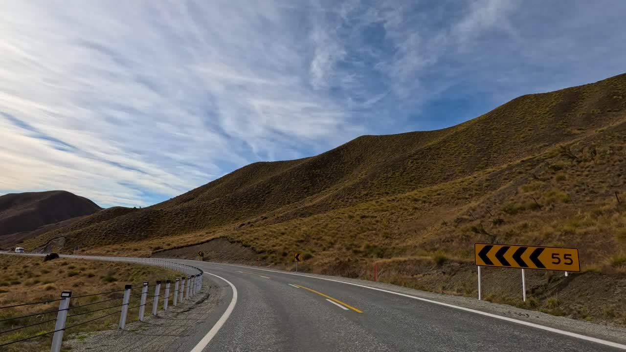 Aerial footage of a winding road through Lake Tekapo's mountainous landscape under a partly cloudy sky