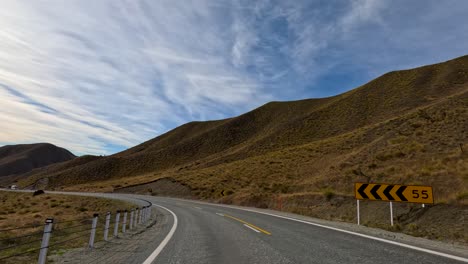 aerial footage of a winding road through lake tekapo's mountainous landscape under a partly cloudy sky