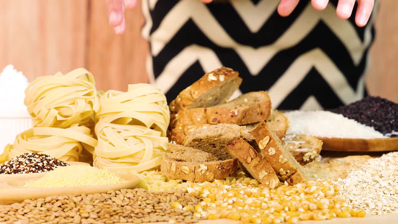 Hands organize various grains and bread slices on a wooden table. Bright lighting enhances the colorful, textured food display
