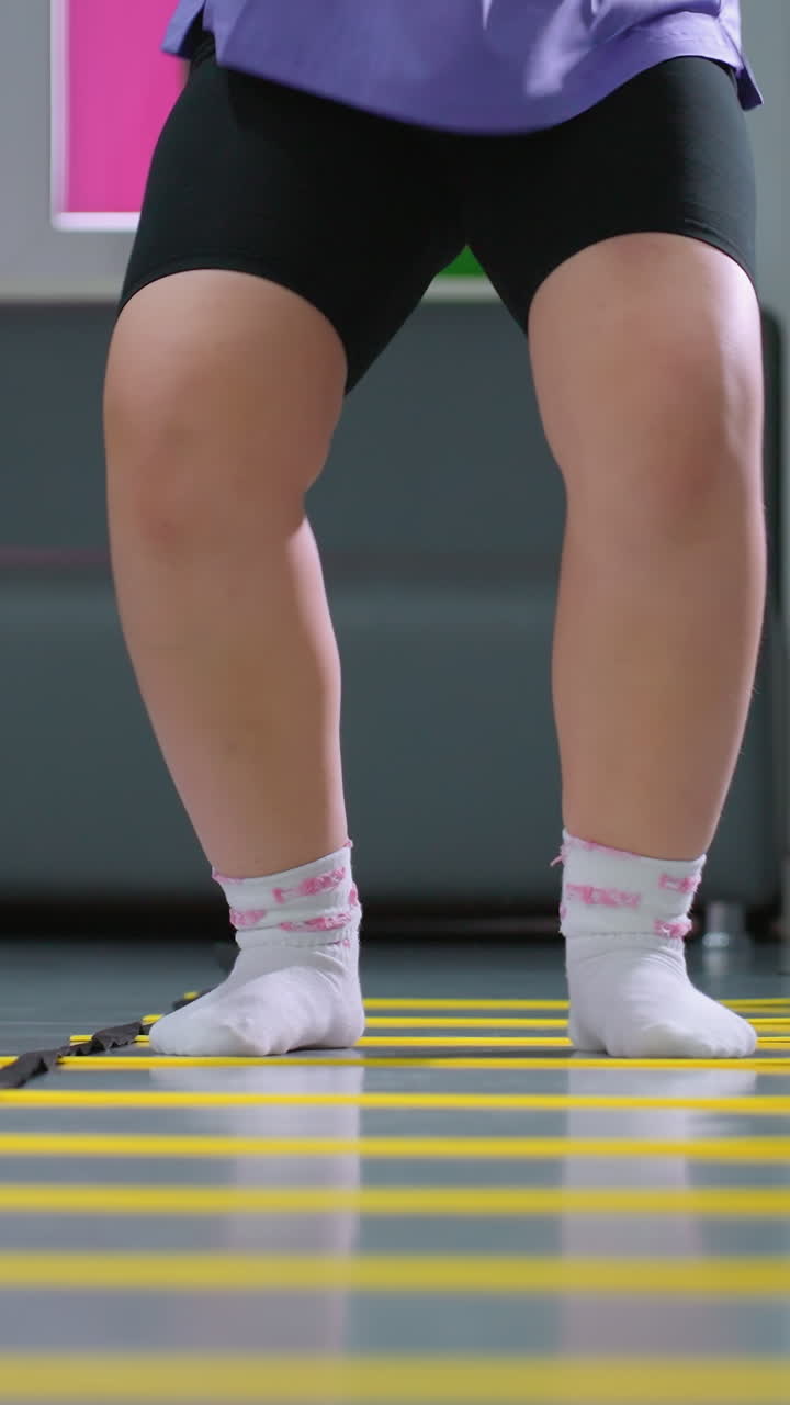 여성 운동 세션의 낮은 각도 뷰, 참가자들이 균형과 체력 훈련을 위해 민한 사다리를 통해 통제된 점프를 수행하는 동안 안정성과 조정에 초점을 맞추고 있습니다.