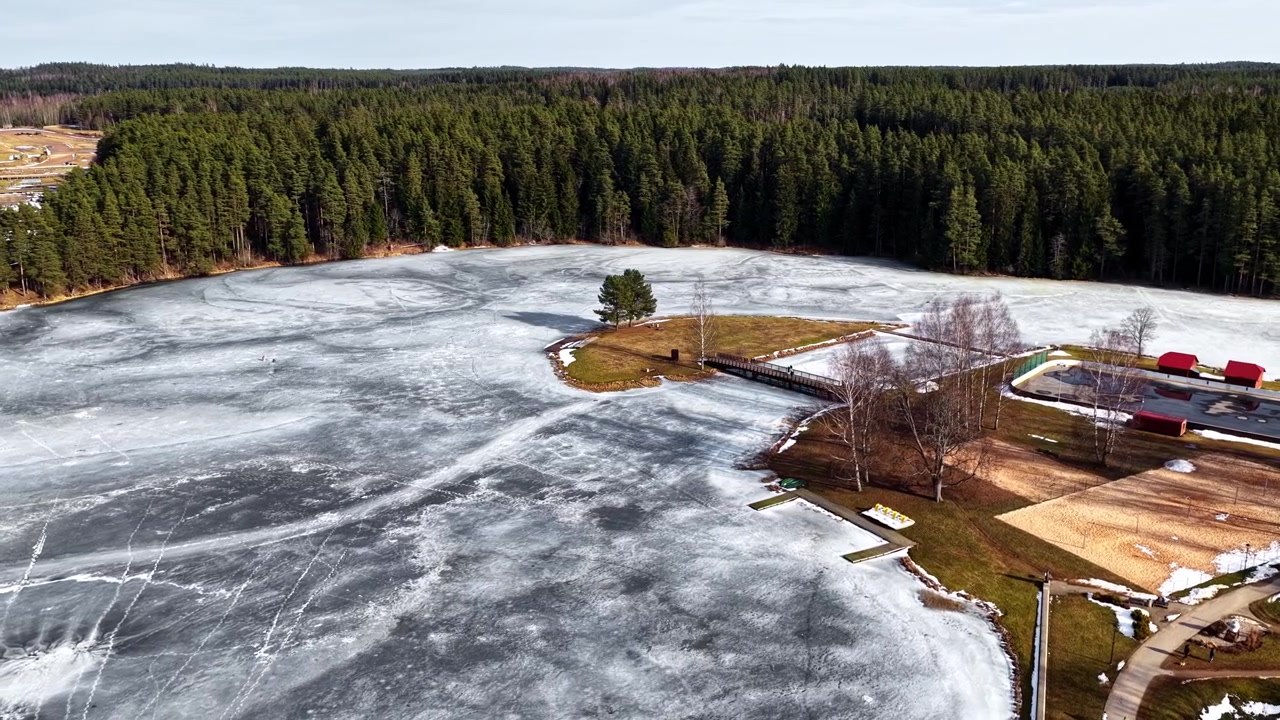 Tající zamrzlé jezero během časného jara s rozsáhlým jehličnatým lesem poblíž z ptačí perspektivy.
