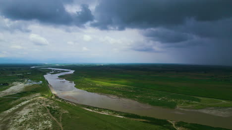 cinematic drone shot of a huge plain land which has river flowing through with greenery surrounded by different vegetation