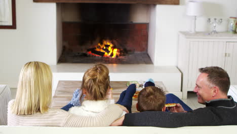 familia sentada en el sofá en el salón al lado del fuego abierto comiendo pizza