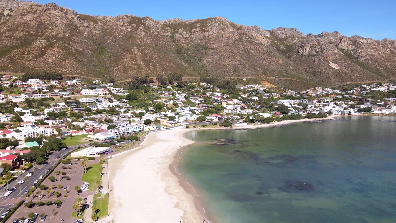 Gordon's Bay, città costiera del Sudafrica: spiaggia principale ai piedi delle scenografiche montagne Hottentots-Holland. Inquadratura di apertura con drone in tilt-up