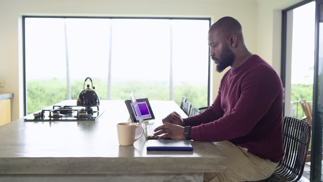 Entering frame man typing on laptop at home counter, sipping coffee, typing again, copy space