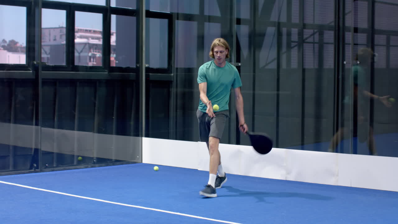 Fokusert mann spiller padeltennis på innendørsbane, holder racketen klar til handling