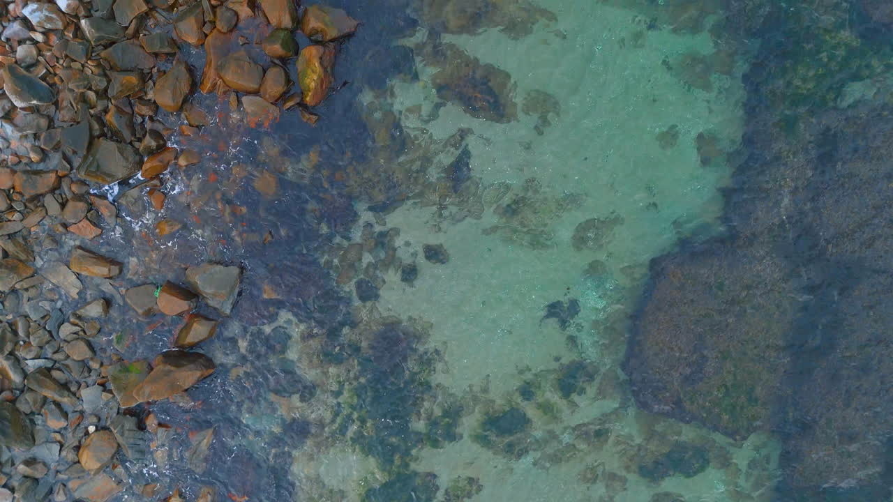 Water meets rocks on a clear day. Shallow water over rocky shorelines. The colors of the water and rocks blend on this sunny day