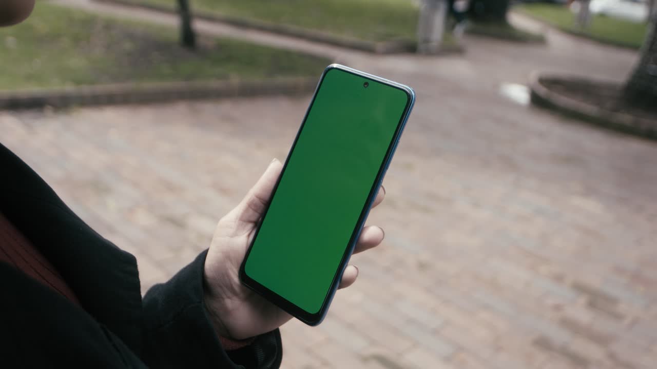 una mujer en traje con cabello rizado camina con un teléfono celular en una pantalla verde en la ciudad de bogotá