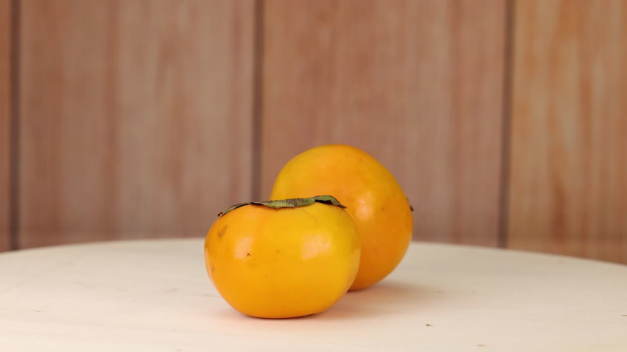 Dua buah kesemek bergulir dan di atas meja