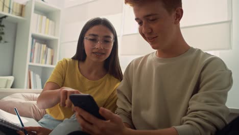 Two-caucasian-teenage-friends-having-fun-while-using-mobile-phones-in-bedroom.