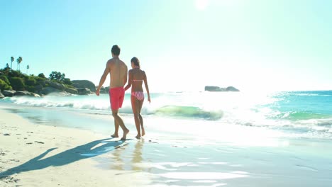 couple holding hands while walking on the beach