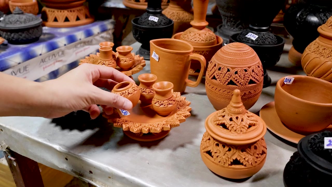 Primer plano de manos examinando cerámicas de barro artesanales expuestas en un mercado local