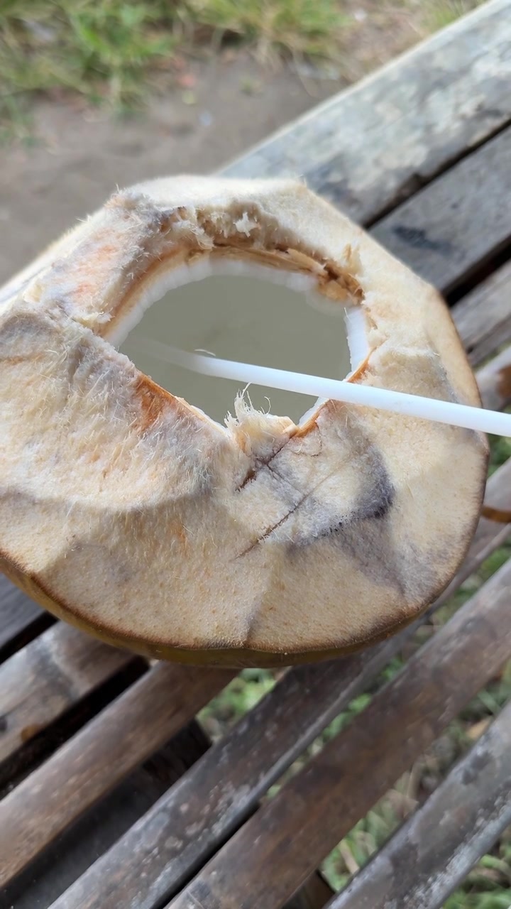Cocco fresco giovane con cannuccia su tavolo di bambù