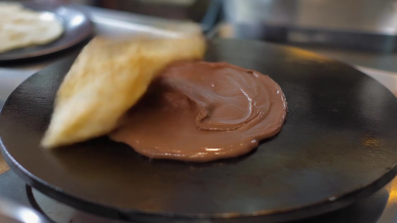 Chef che prepara crêpe al cioccolato su piastra calda