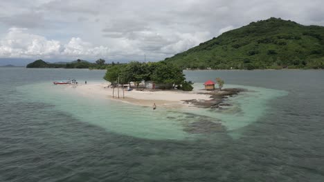 Male-tourist-walks-into-clear-water-from-sand-beach-as-aerial-orbits