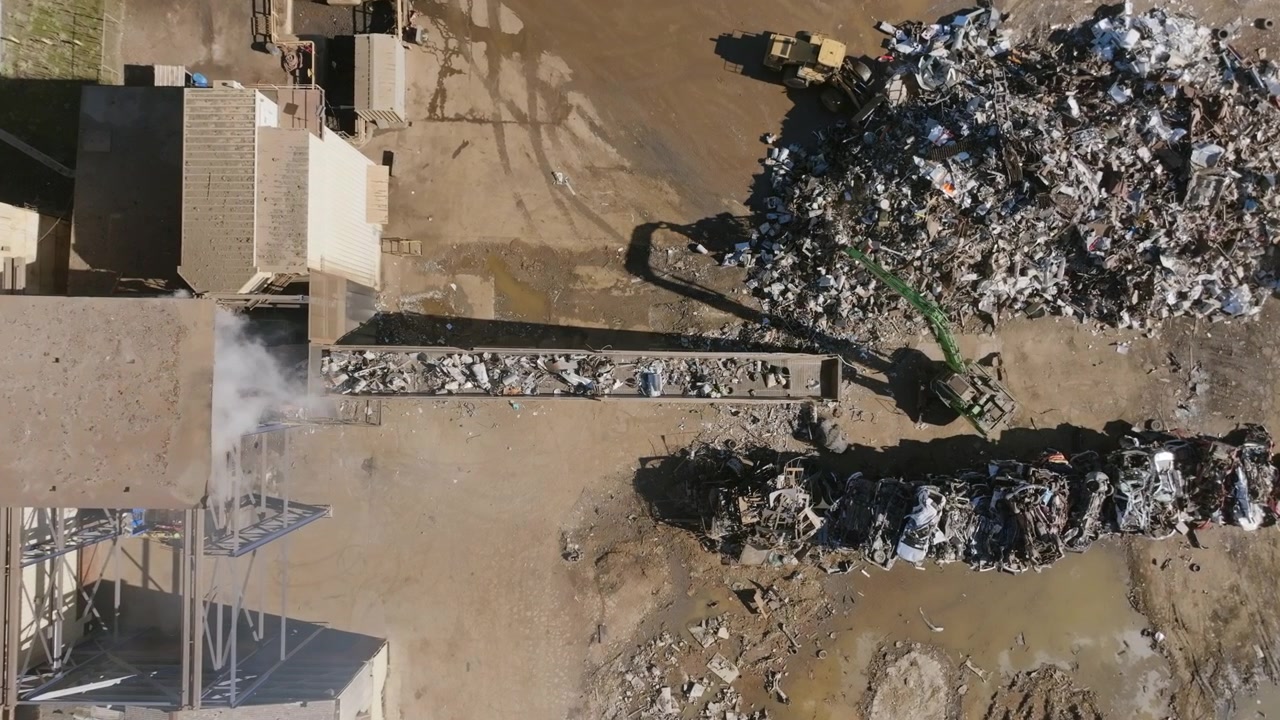 Filmato aereo statico dall'alto con ripresa ravvicinata di una terna che sposta rottami metallici su un nastro trasportatore in un impianto di riciclaggio di metalli.