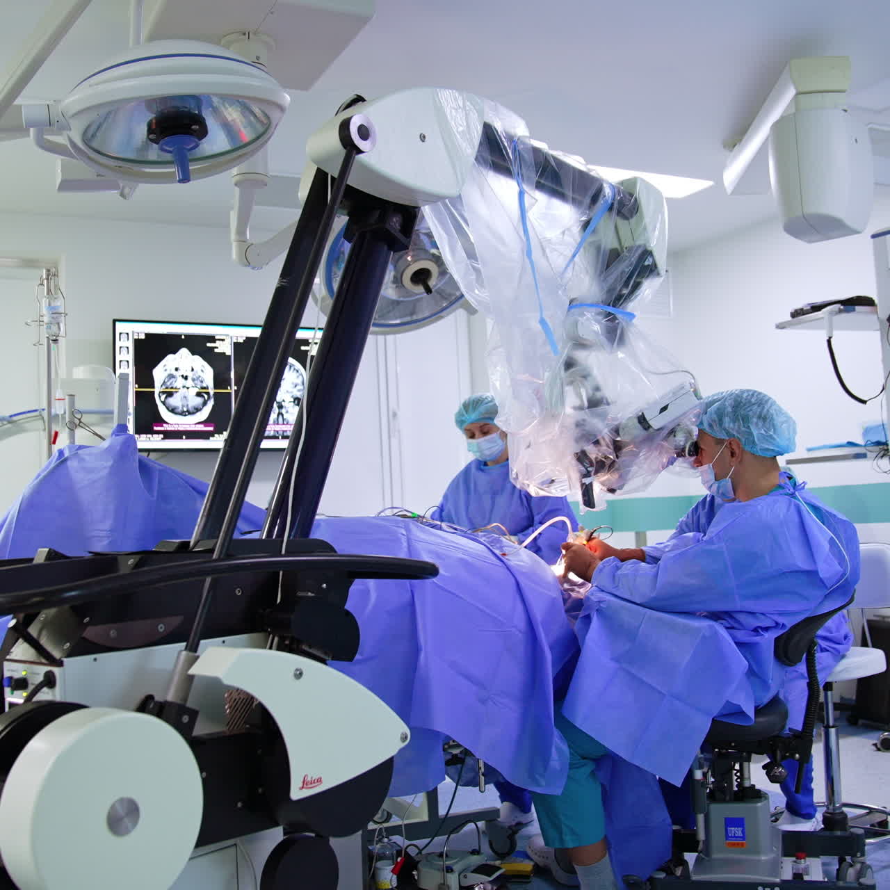 Medical team working in modern well-equipped surgery room. Neurosurgeon looks at microscope operating the patient.