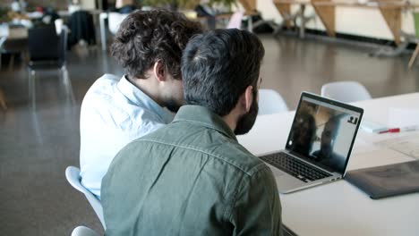 Back-view-of-two-men-having-conversation-through-laptop