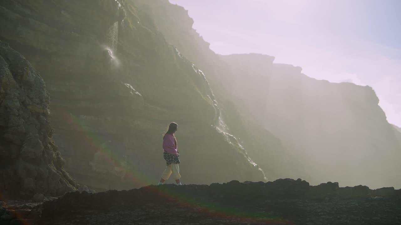 Donna in piedi su una riva rocciosa con cascata e scogliere nebbiose