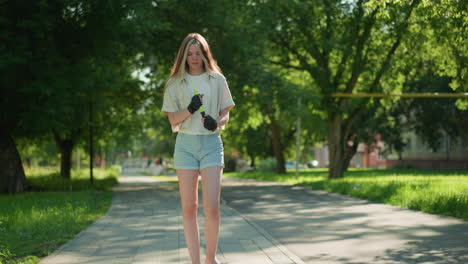 young lady strolls in sunlit park, carefully examining green air pump in hands, sunlight reflects off her as she walks, with blurred figures in distance and lush trees