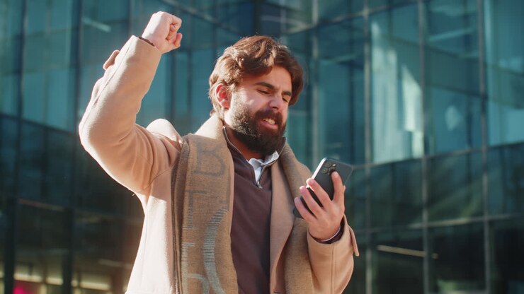 Uomo indiano felice usa uno smartphone per festeggiare una vittoria o una buona notizia in strada, nel centro della città