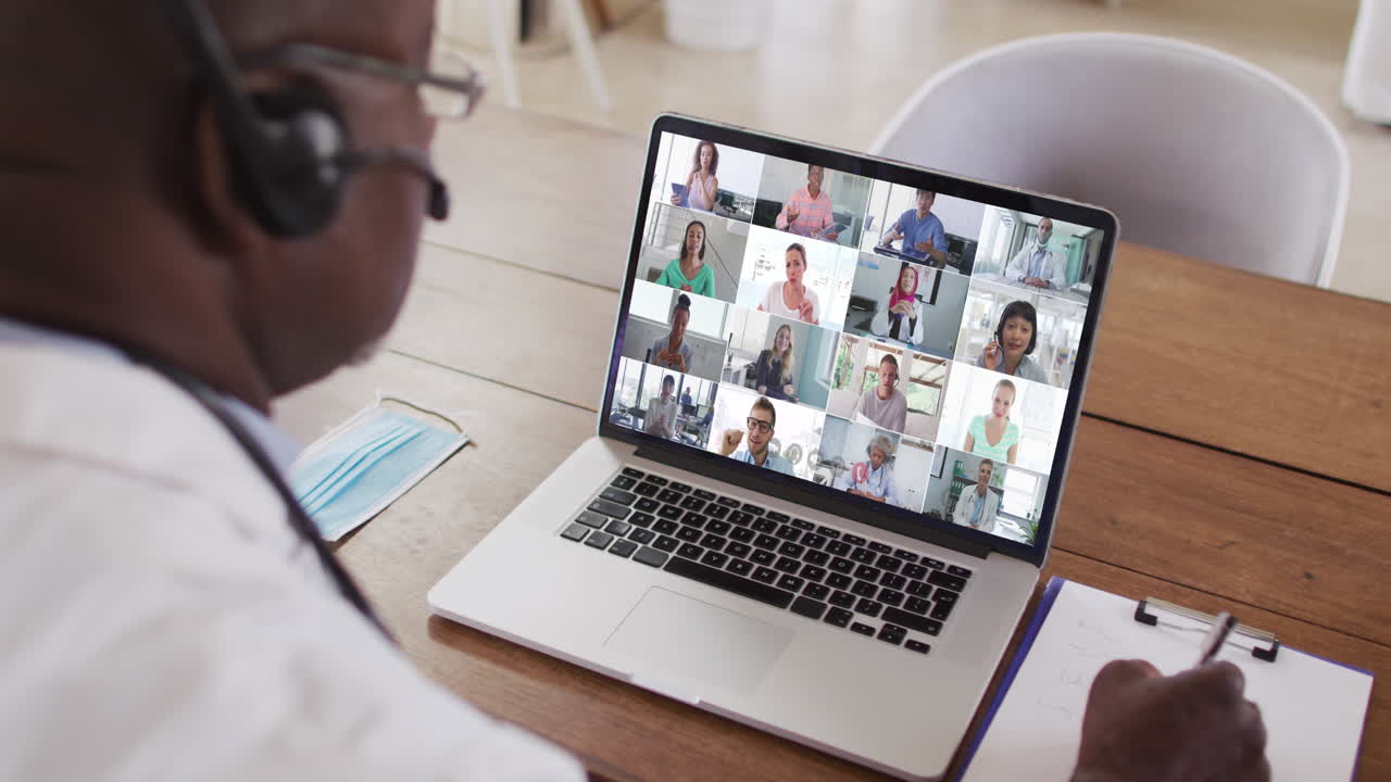 African american male doctor taking notes while having a video conference on laptop