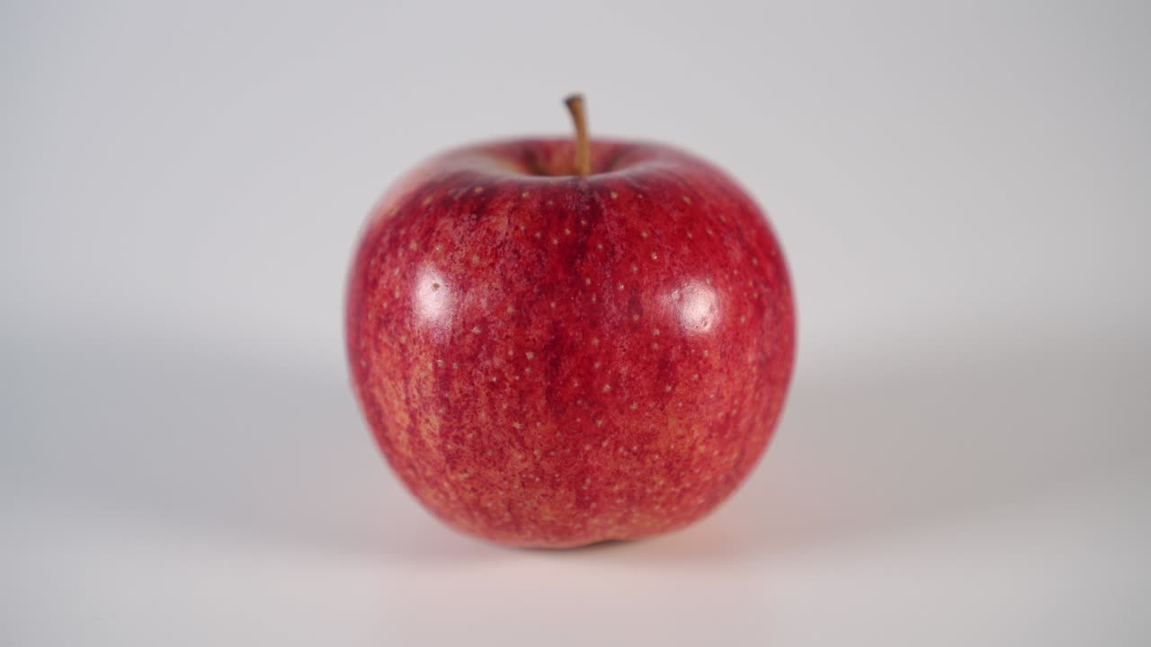 En mand sætter et modent rødt æble på et hvidt bord