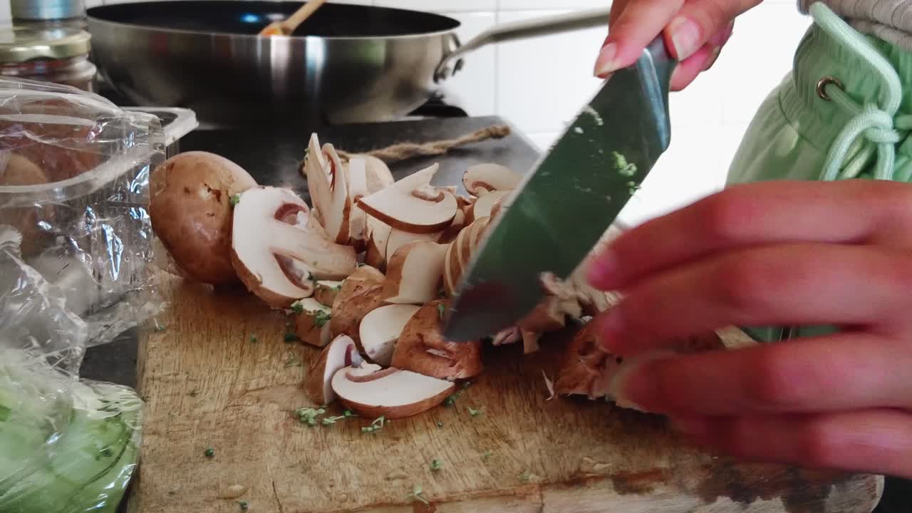 woman in home kitchen cutting champignon mushrooms on wooden cutting board