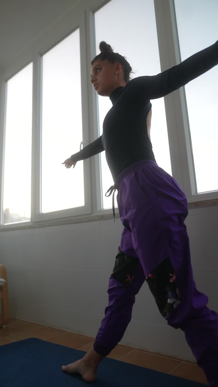 Giovane donna che pratica posizioni di danza o yoga in una stanza moderna