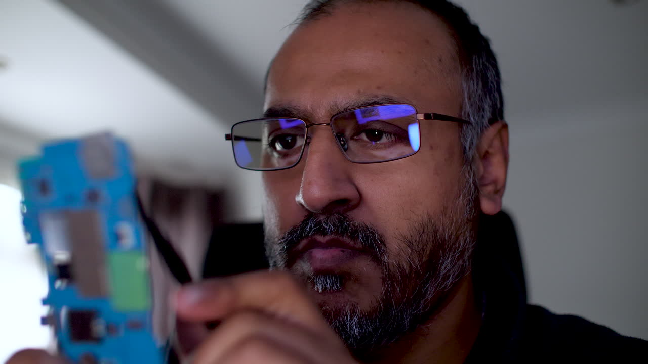 An IT engineer is inspecting a blue motherboard testing its components The technology professional is examining the circuit board for functionality and performance