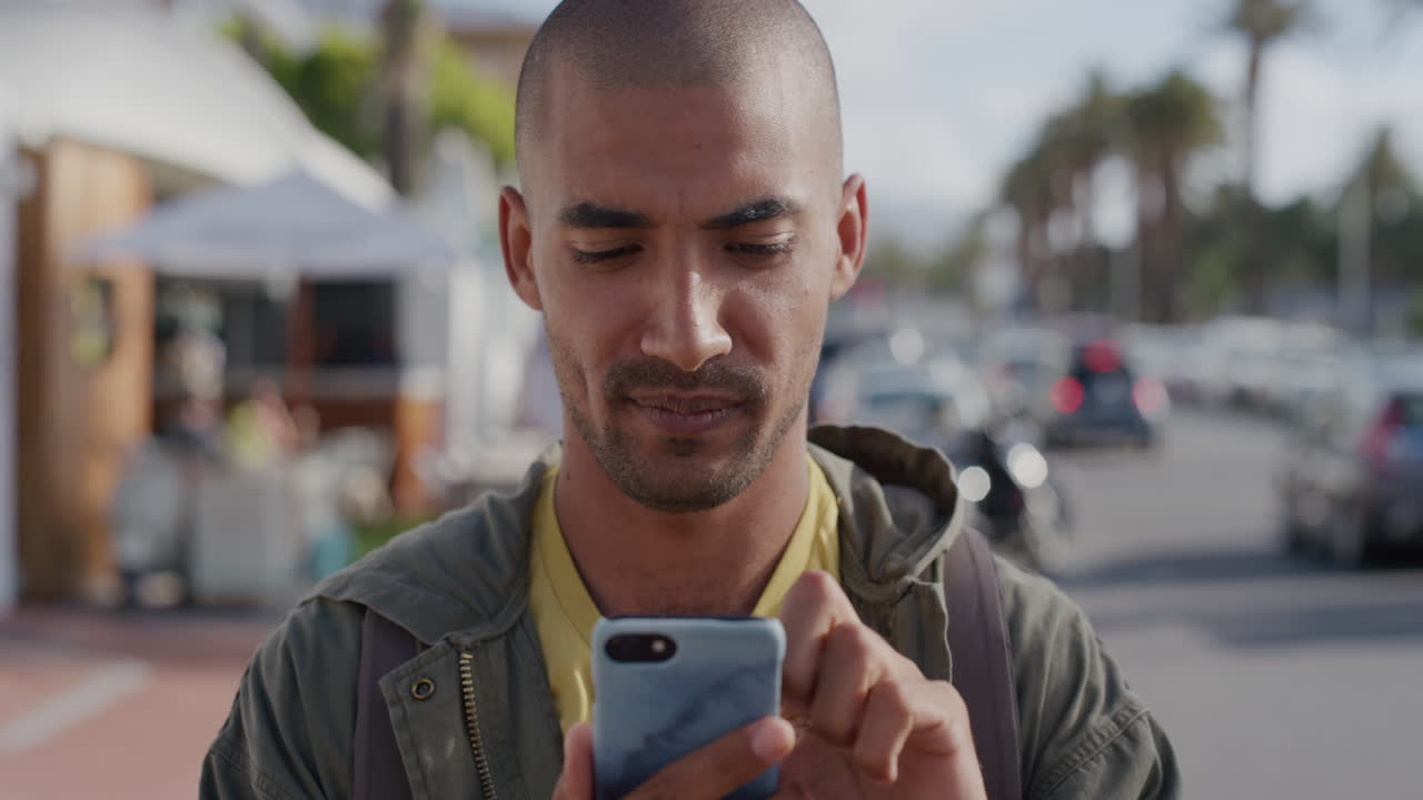 portrait of young hispanic man using smaartphone texting rbwosing sending sms sharing summer vacation experience enjoying vibrant sunny urban city street