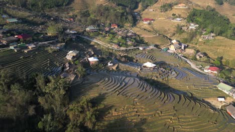 Aerial-drone-shot-of-villages-amdist-bright-green-rice-terraces-in-the-mountains-of-Sapa,-Vietnam