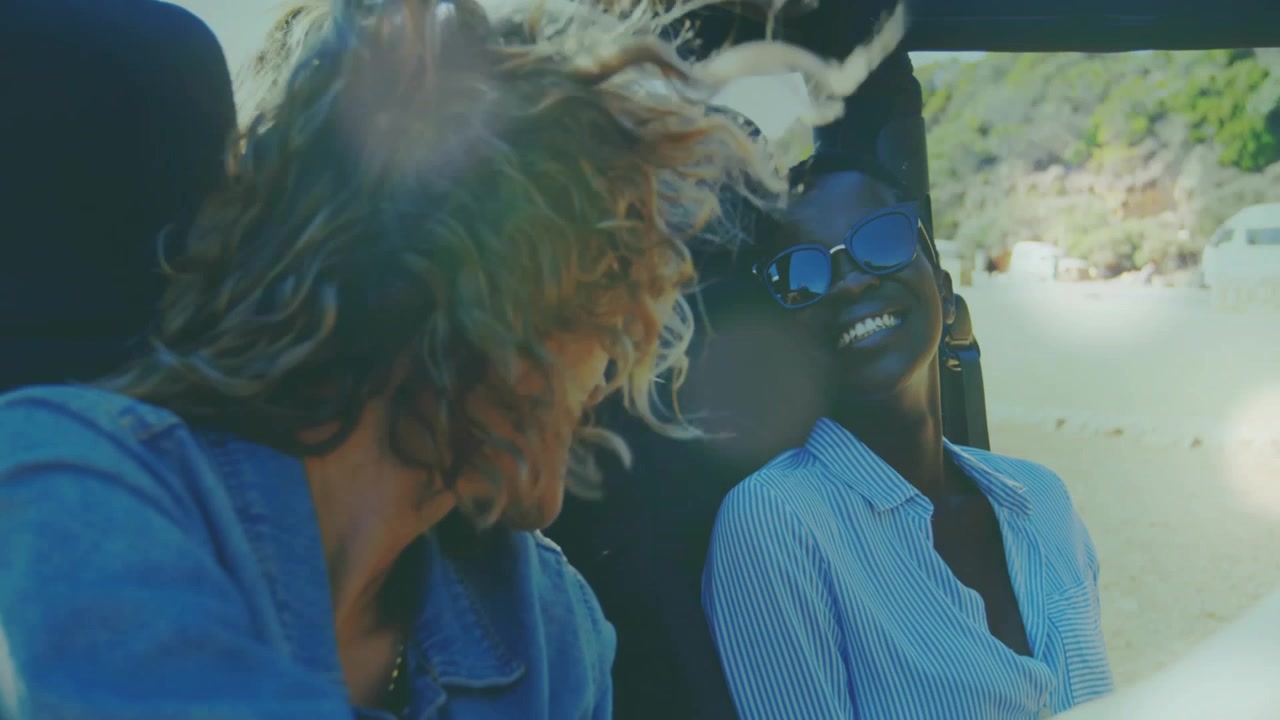 Dos adultos girando y sonriendo en un vehículo descapotable mientras el viento les despeina el cabello, de viaje